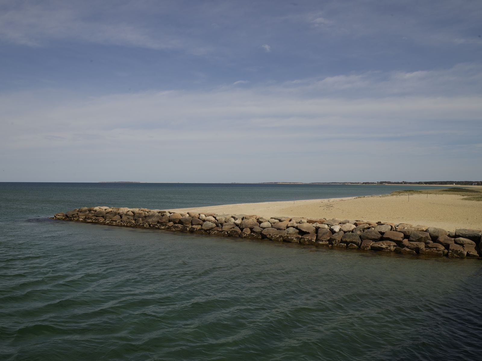 Calm water meeting a low rocky spit on a quiet shoreline
